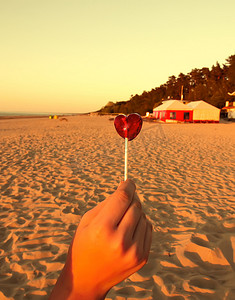 沙滩背景上手里拿着一颗心形的红色糖果。