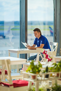 在机场咖啡厅等候登机时使用笔记本电脑工作的年轻人