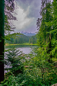 在一个美丽的清楚的湖的灰色阴暗天空以绿色山小山为背景