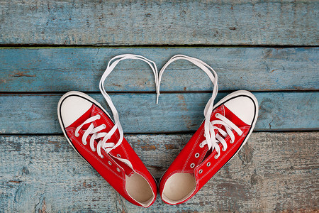 红色复古背景摄影照片_蓝色木质背景上的一双红色复古运动鞋，鞋带