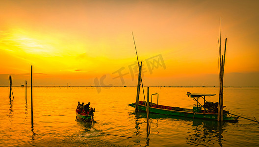 泰国日落时，渔夫的船漂浮在竹竿附近的海中。