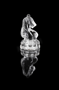 国际象棋骑士摄影照片_黑色孤立背景上的玻璃国际象棋骑士。