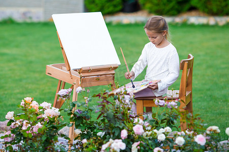 可爱的小女孩在户外温暖的日子里在画架上画画