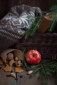 打开的旧书摄影照片_圣诞树树枝上的红黄苹果，靠近篮子，上面放着羊毛衫和一本旧书