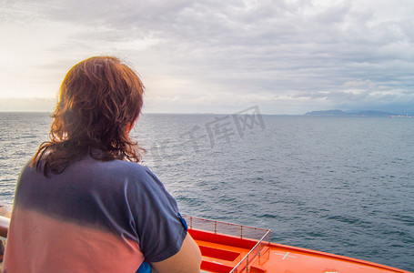 快乐之旅摄影照片_快乐的女人看着海岸线和大海，享受游轮之旅，从后面欣赏美景