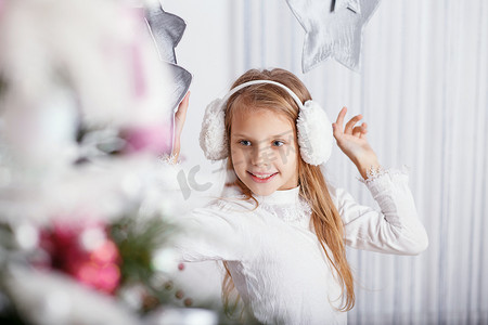 漂亮的小女孩戴着耳罩装饰圣诞树