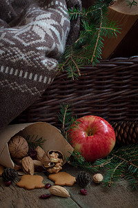 黄苹果摄影照片_圣诞树树枝上的红黄苹果，靠近篮子，上面放着羊毛衫和一本旧书