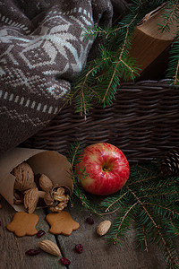 黄苹果摄影照片_圣诞树树枝上的红黄苹果，靠近篮子，上面放着羊毛衫和一本旧书