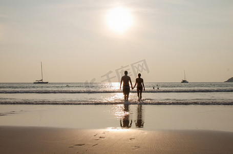 日落时牵手走在沙滩上的情侣剪影。