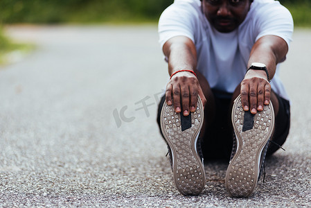 戴手表摄影照片_运动跑步者黑人戴手表他坐着拉脚趾脚伸展腿和膝盖
