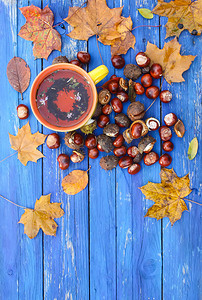 黄色陶瓷杯凉茶在年迈的木背景与秋天秋叶和栗子。