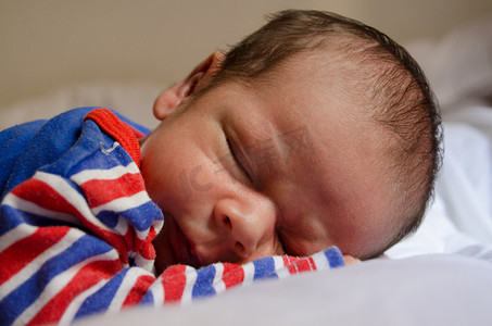 红色大嘴唇摄影照片_两周大的新生男婴穿着蓝色红色睡衣睡觉