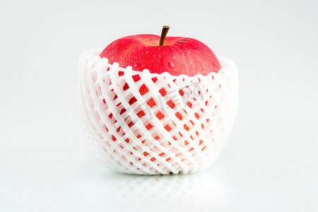 一个红苹果，皮肤上有水滴，白色防震泡沫网包裹在白色背景上，带有复制空间。