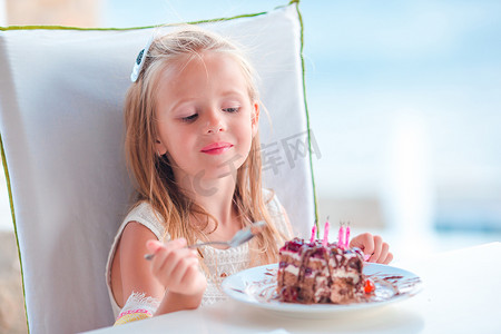 生日快乐庆祝蛋糕摄影照片_小女孩在户外咖啡馆用美味的蛋糕庆祝生日快乐