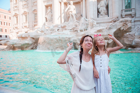 旅行的家庭妈妈和女孩在意大利罗马的特雷维喷泉投掷硬币以求好运。
