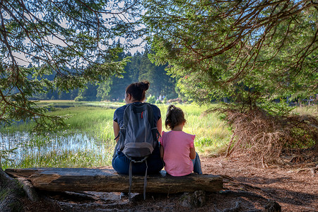 国朝山水插画摄影照片_母亲和女儿坐在山湖附近的长椅上，面朝远处