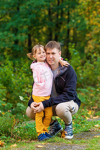 .一个手臂骨折的女孩在秋天散步时在一个旧公园里拥抱她的父亲
