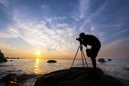 摄影师摄影照片_在岩石上拍摄日出照片的摄影师剪影，
