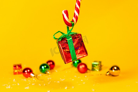 糖果手杖棒棒糖拿着一个礼盒，里面有黄色背景的圣诞礼物，圣诞糖果和新年装饰