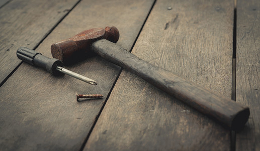 老生锈的锤子、螺丝刀和钉子在老木桌上。