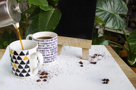 白色背景和植物背景上的热咖啡、咖啡豆和空黑板，工作室拍摄。