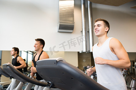 朋友跑步摄影照片_微笑的男人在健身房的跑步机上锻炼