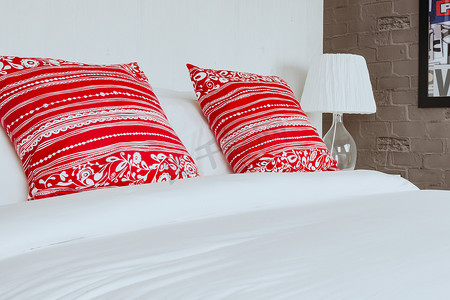 红色毛毯和枕头摄影照片_在卧室的红色枕头有白色床单和灯的