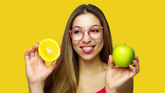 美味吐舌头摄影照片_正面明亮的漂亮女人微笑着吐舌头，拿着美味的水果，看着一边。
