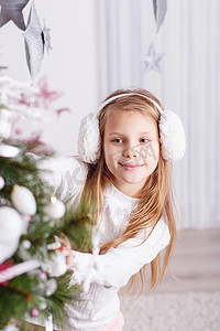 友谊装饰摄影照片_漂亮的小女孩戴着耳罩装饰圣诞树
