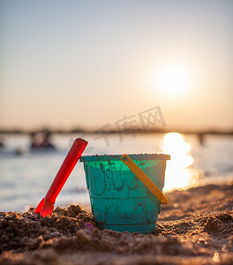 塑料桶摄影照片_沙滩上玩耍的儿童玩具、岸上的水桶和耙子