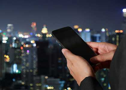 女性手持和触摸屏智能手机，手机在模糊抽象的夜城背景下作为创新概念。
