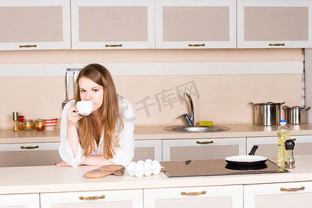 早上，女孩一件白人男式衬衫正在厨房的桌子上喝茶肘