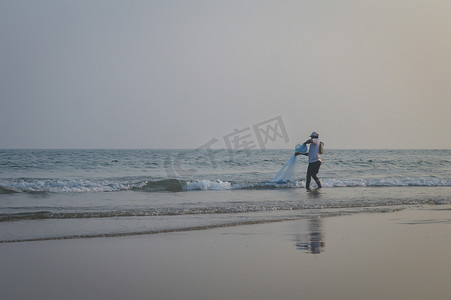 男渔夫在一个夏日的傍晚用渔网捕鱼，这是印度海岸小渔村的传统捕鱼方式。