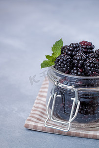 新鲜黑莓和带薄荷叶的覆盆子的特写，放在质朴餐桌上的玻璃罐中