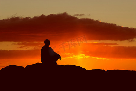 坐在海边摄影照片_夕阳下坐在海边岩石上沉思的家伙