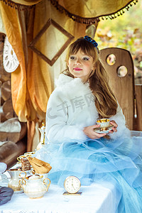 爱丽丝梦游仙境风景中的小美女桌前端着一杯茶的正面图