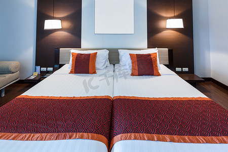 红色毛毯和枕头摄影照片_在双人卧室的红色枕头有白色床单和灯的