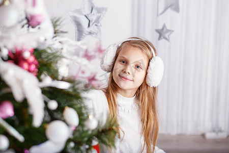 漂亮的小女孩戴着耳罩装饰圣诞树
