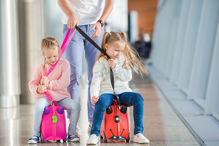 在机场玩得开心的可爱小女孩坐在手提箱上等待登机