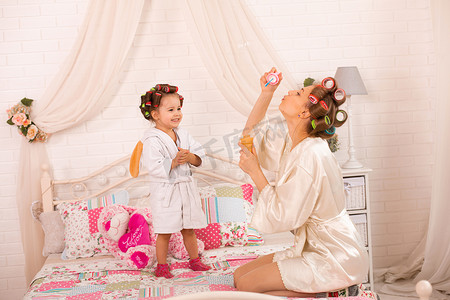 卷发机摄影照片_一个迷人的小女孩和她妈妈戴着卷发器玩肥皂球。