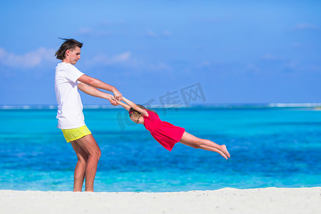 家庭度假摄影照片_热带海滩度假期间可爱的小女孩和爸爸