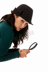 睿智的人摄影照片_戴着放大镜和帽子的年轻女子看着白色背景中突显的相机