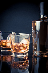 蓝色瓶子摄影照片_在黑色背景和浅蓝色的瓶子附近的玻璃杯中加冰的威士忌