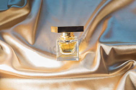 .金色折叠丝织物背景上的香水瓶。