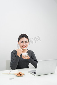 美丽的亚洲女商人坐在家里的工作地点，边吃酸奶边微笑