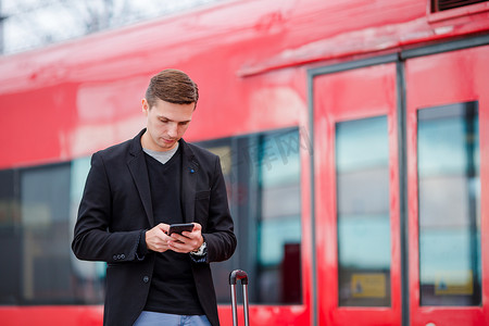 年轻的白人男子带着智能手机和行李在车站乘火车旅行