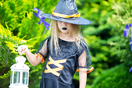 万圣室外摄影照片_快乐的小女孩在万圣节户外穿着女巫服装。