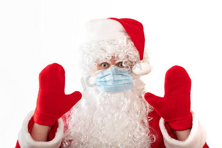 一个身穿圣诞老人服装、戴着医用面具、双手举起、睁大眼睛，仿佛在警告或阻止某事的男子，在白色背景中被隔离。
