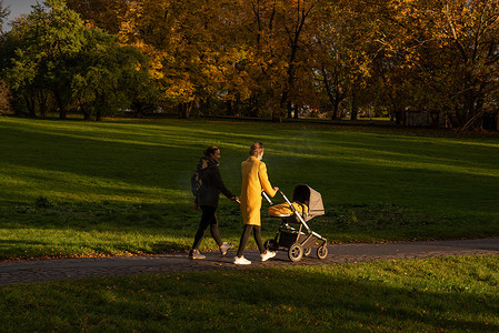 两个朋友在公园里散步，一个带着婴儿推车
