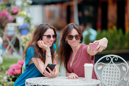 女性电话摄影照片_两个年轻女孩在户外咖啡馆用智能手机自拍。